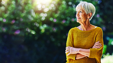 Senior woman in yellow sweater standing in front of a tree crossing her arms